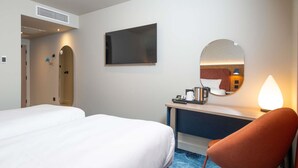 Ein Hotelzimmer mit zwei Betten, einem Schreibtisch, einem Stuhl, einem Spiegel und einer Kaffeemaschine.
