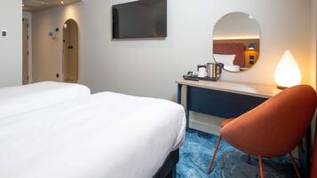A hotel room with two beds, a desk, a chair, a mirror, and a coffee maker.