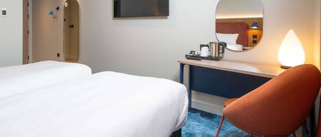 Ein Hotelzimmer mit zwei Betten, einem Schreibtisch, einem Stuhl, einem Spiegel und einer Kaffeemaschine.