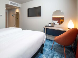 Habitación de hotel con dos camas, un escritorio, una silla, un espejo y una cafetera.