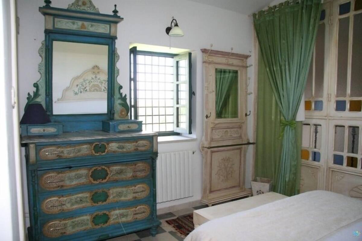 A bedroom with a bed, a dresser, a mirror, a window with a view, and a cabinet.
