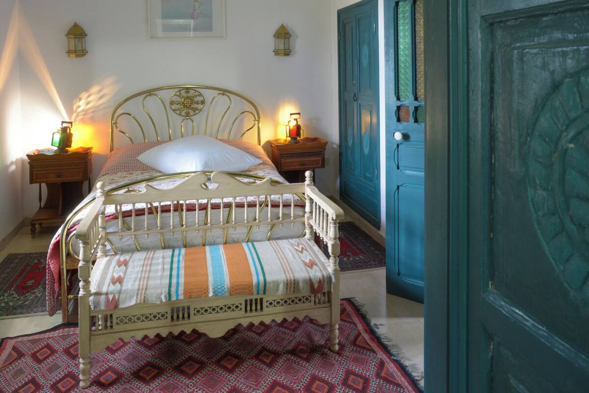 A bedroom with a bed, two bedside tables, a nightstand, a door, and a wall-mounted picture.