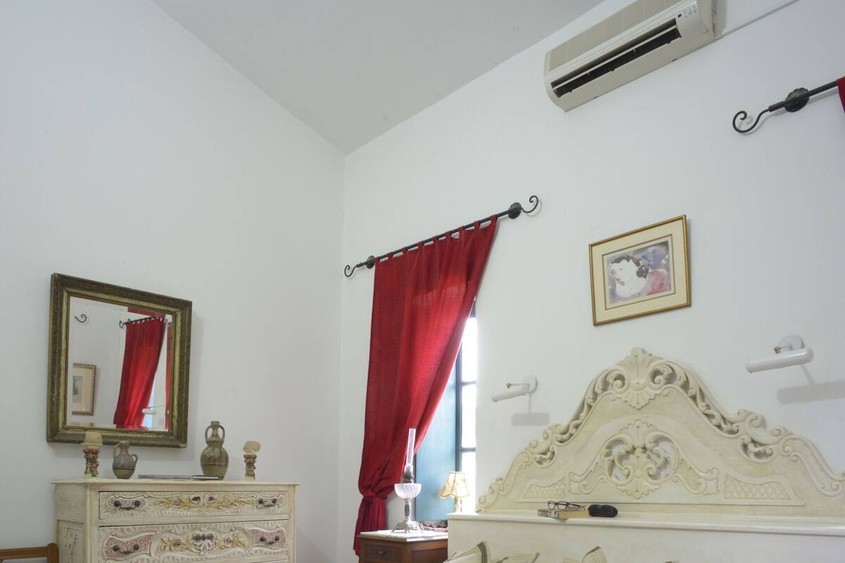 A bedroom with a bed, dresser, mirror, and an air conditioning unit.
