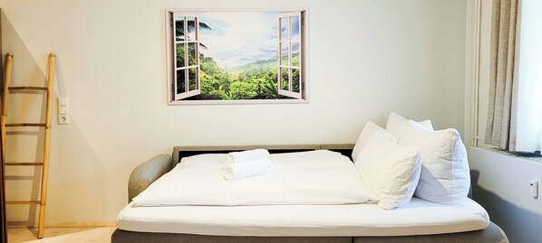 A neatly made bed with white linens and pillows, a framed picture of a tropical landscape, a wooden ladder, and a window with curtains.