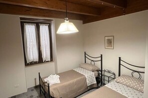 Un dormitorio con dos camas individuales, una ventana con cortinas, una lámpara colgante y un cuadro pequeño en la pared.