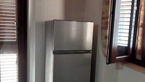 Un réfrigérateur en acier inoxydable dans une cuisine dotée d’une fenêtre et de stores.