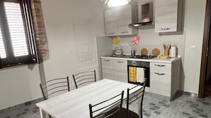 Une cuisine de taille réduite comprenant une table et des chaises, un fourneau et une fenêtre avec des stores.
