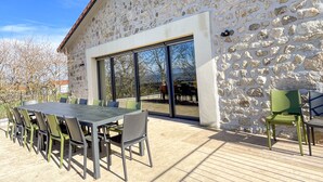 A stone building with a tiled roof, a large glass door, and an outdoor patio with a table and chairs. - Gîte des Ollières : Entre Charme Traditionnel et Confort Moderne (Monistrol-sur-Loire)