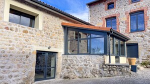 A stone building with large windows and a gravel driveway. - Gîte des Ollières : Entre Charme Traditionnel et Confort Moderne (Monistrol-sur-Loire)