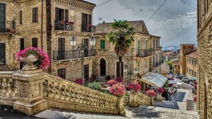 A historic stone building with a balcony, a palm tree, and a staircase leading to the entrance. - Ferruccio's House - Ground Floor (Colonnella)