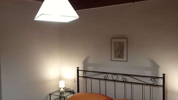 A bedroom with a metal bed frame, two pillows, a bedside table with a lamp, and a framed picture on the wall. - Ferruccio's House - Ground Floor (Colonnella)