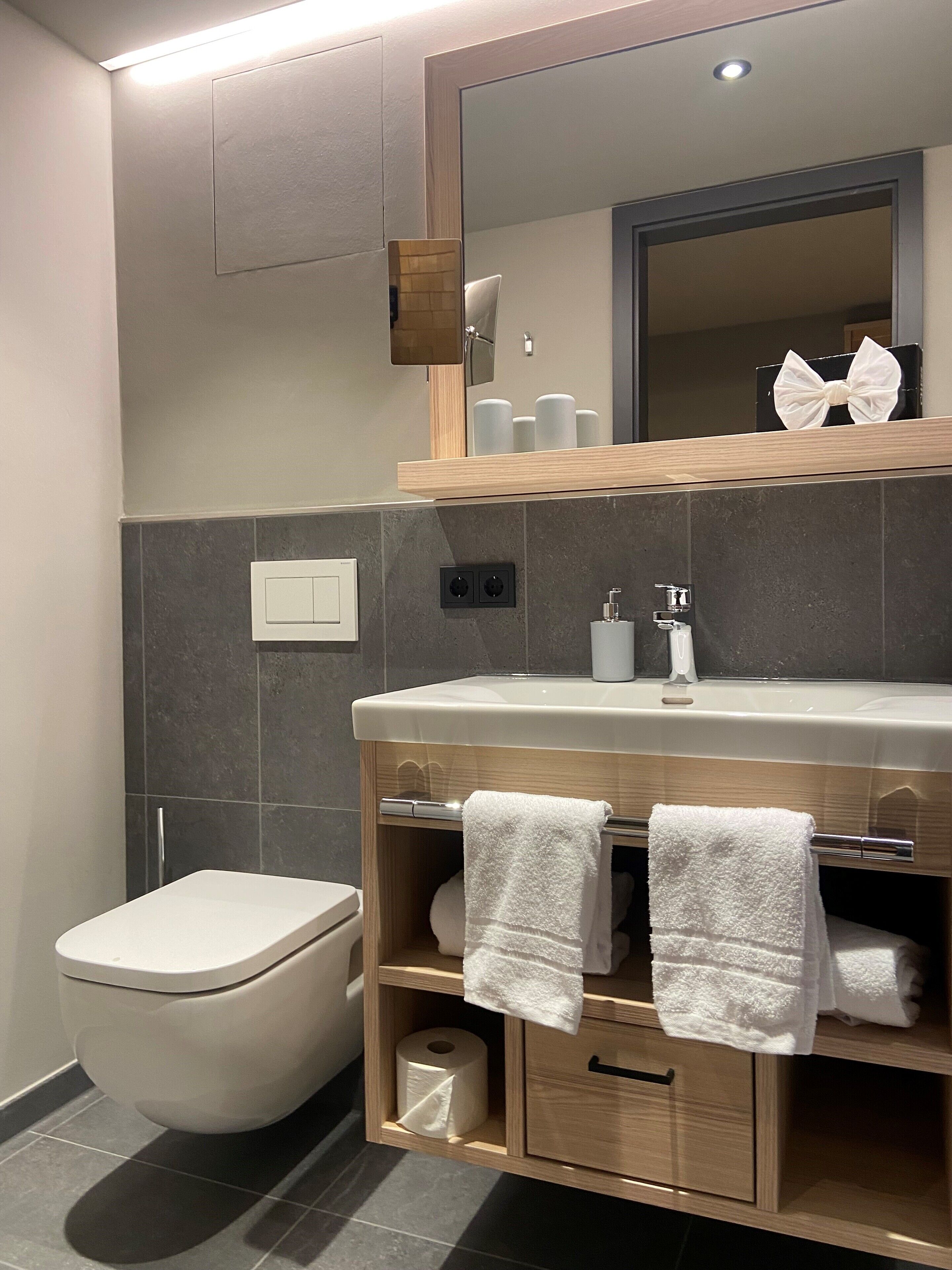 A modern bathroom with a toilet, a vanity with a mirror, and a shelf with toiletries.
