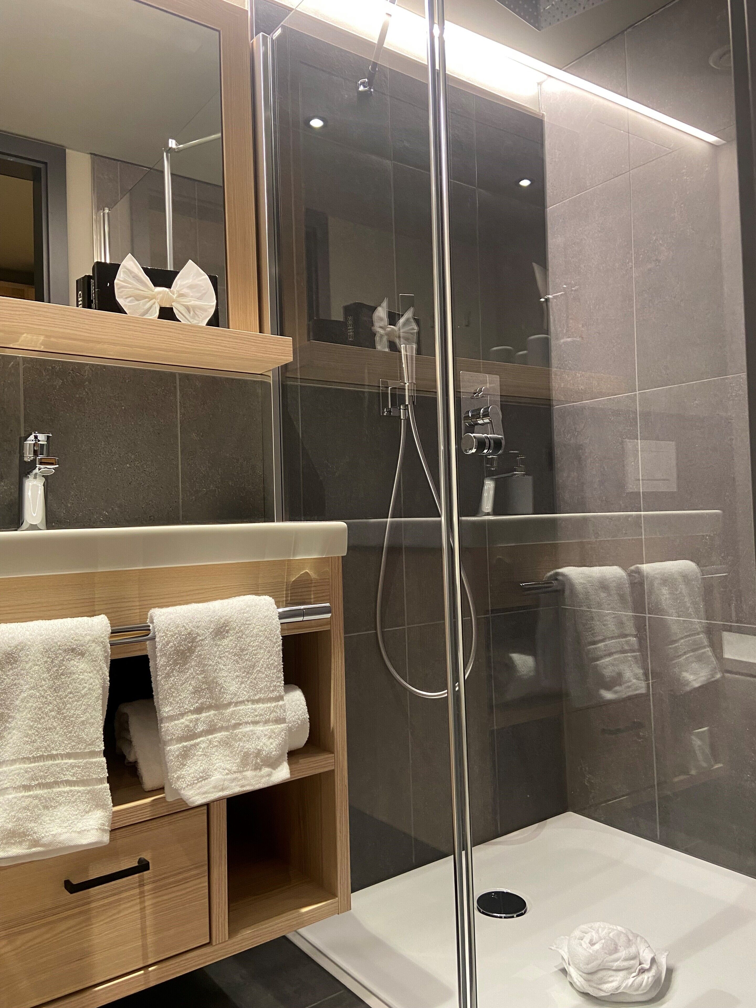 A modern bathroom with a glass-enclosed shower, a wooden vanity with a mirror, and a white bathtub.
