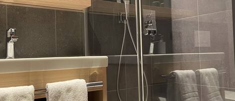 A modern bathroom with a glass-enclosed shower, a wooden vanity with a mirror, and a white bathtub.