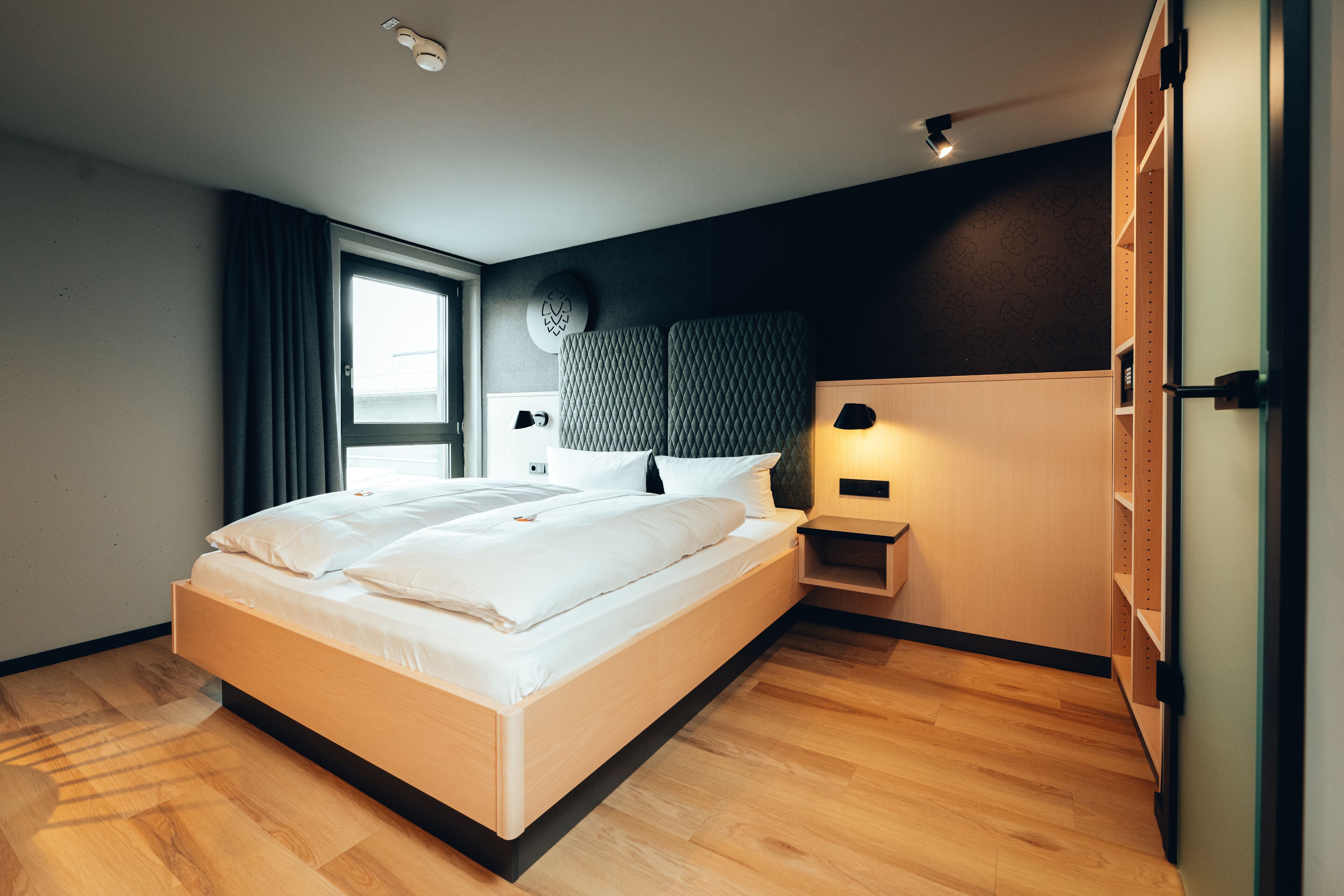 Ein modernes Schlafzimmer mit einem hölzernen Bett, einem Nachttisch, einer Wandleuchte und einem Kleiderschrank.