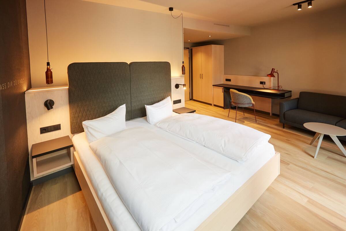 A modern hotel room with a large bed, a desk, and a seating area.