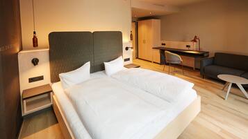 A modern hotel room with a large bed, a desk, and a seating area.