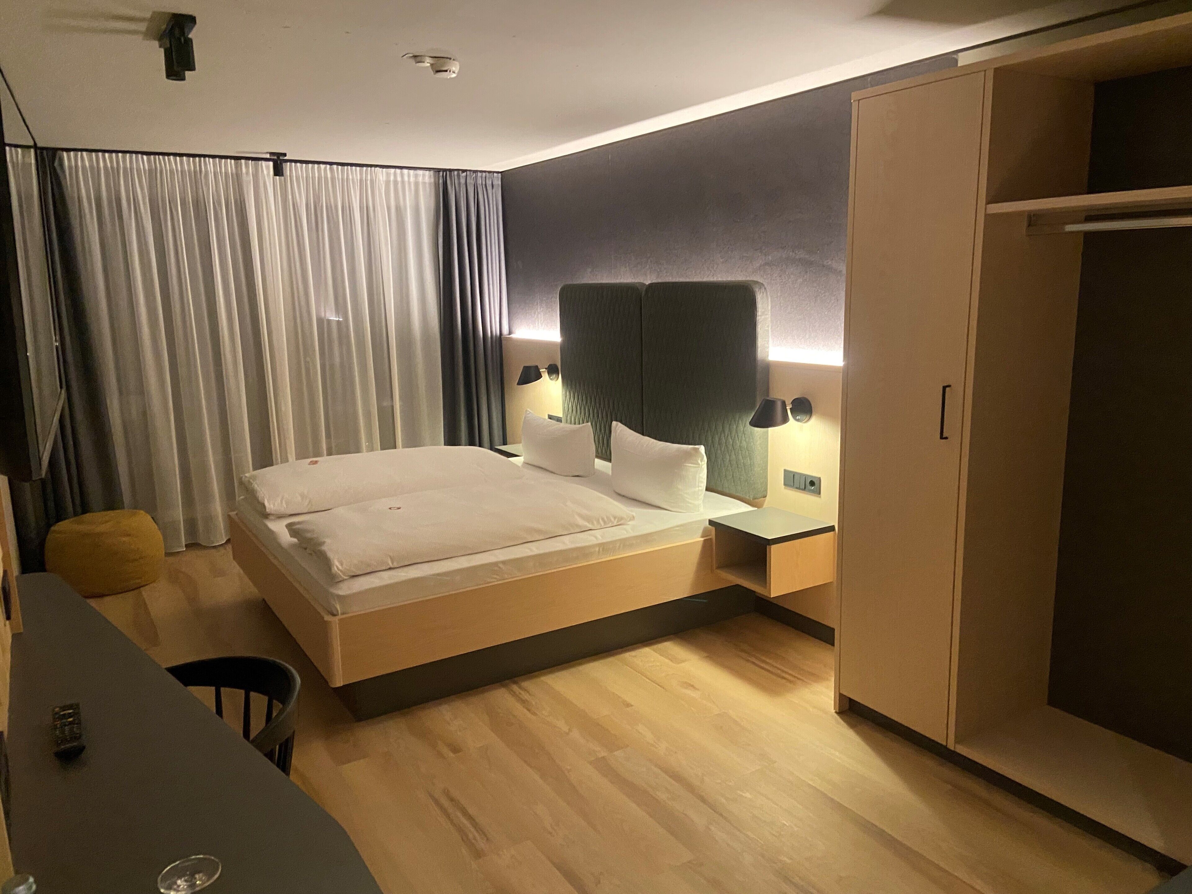 Une chambre d’hôtel moderne avec un grand lit, des tables de chevet, une armoire et un bureau avec une chaise.