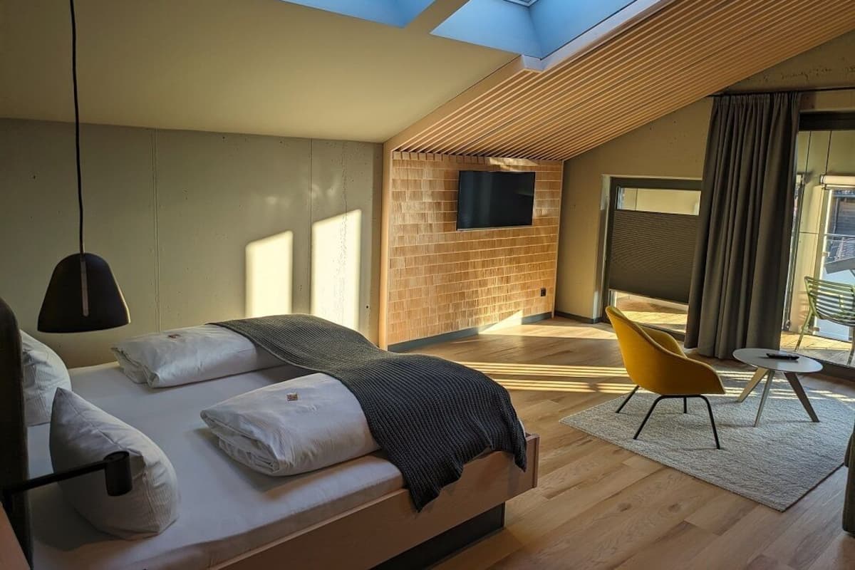A modern bedroom with a skylight, a bed, a TV, and a yellow chair.