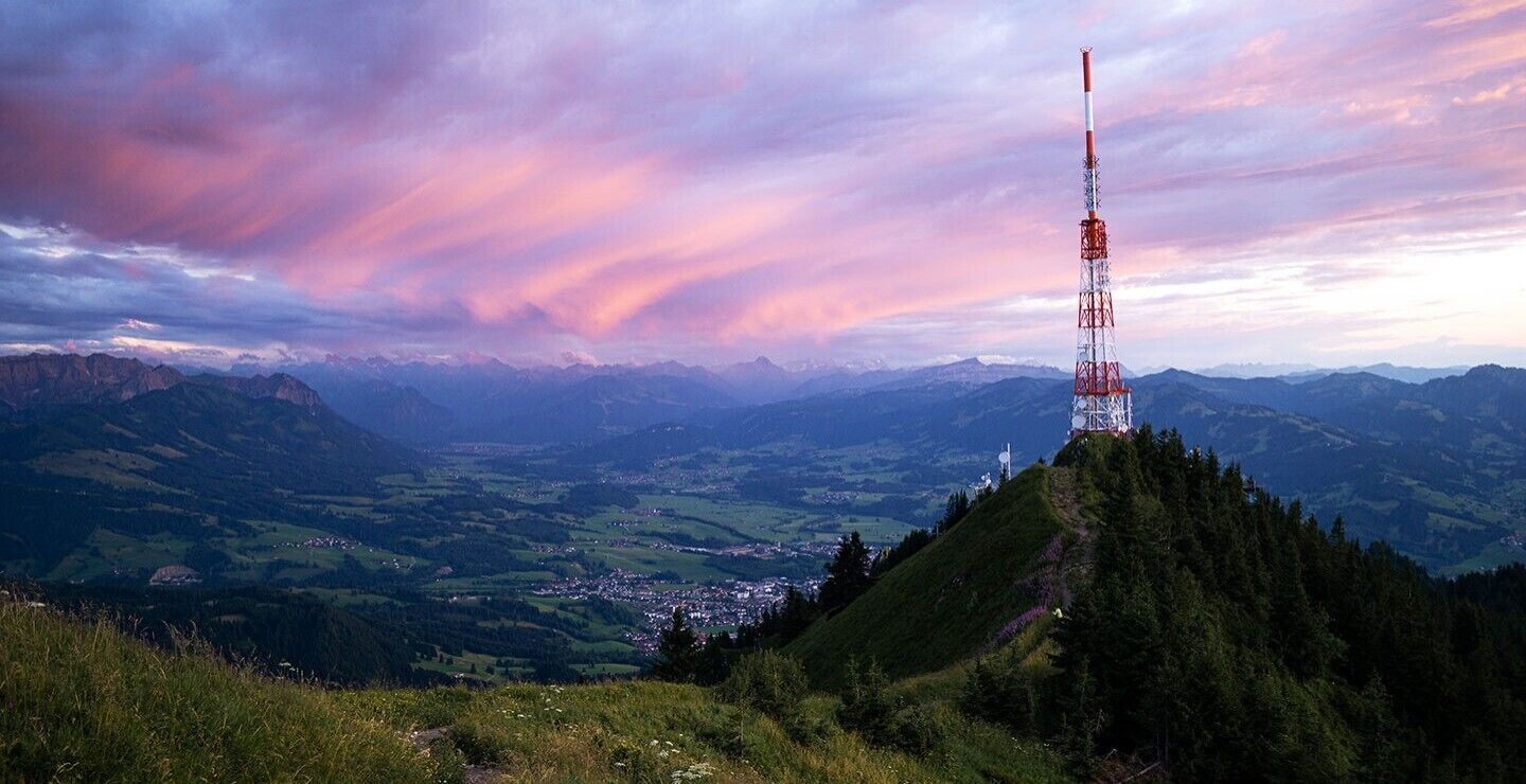 A telecommunications tower on a mountain peak with a town in the valley below.