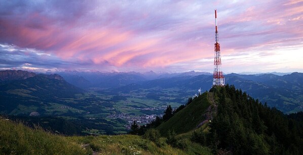 Ein Mobilfunkturm auf einem Berggipfel, darunter liegt eine Stadt im Tal.
