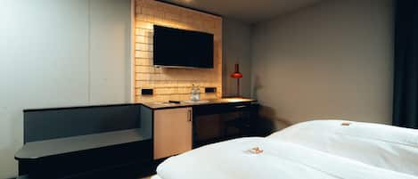 A modern hotel room with a bed, a desk, a TV mounted on a wooden panel, and a red floor lamp.