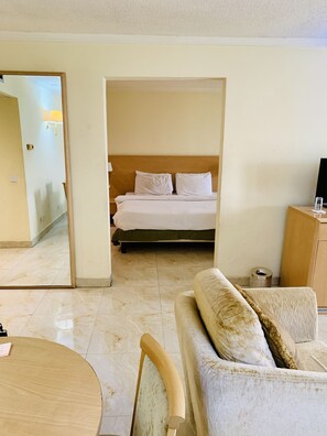 A hotel room with a bed, a sofa, a small table, and a mirror.