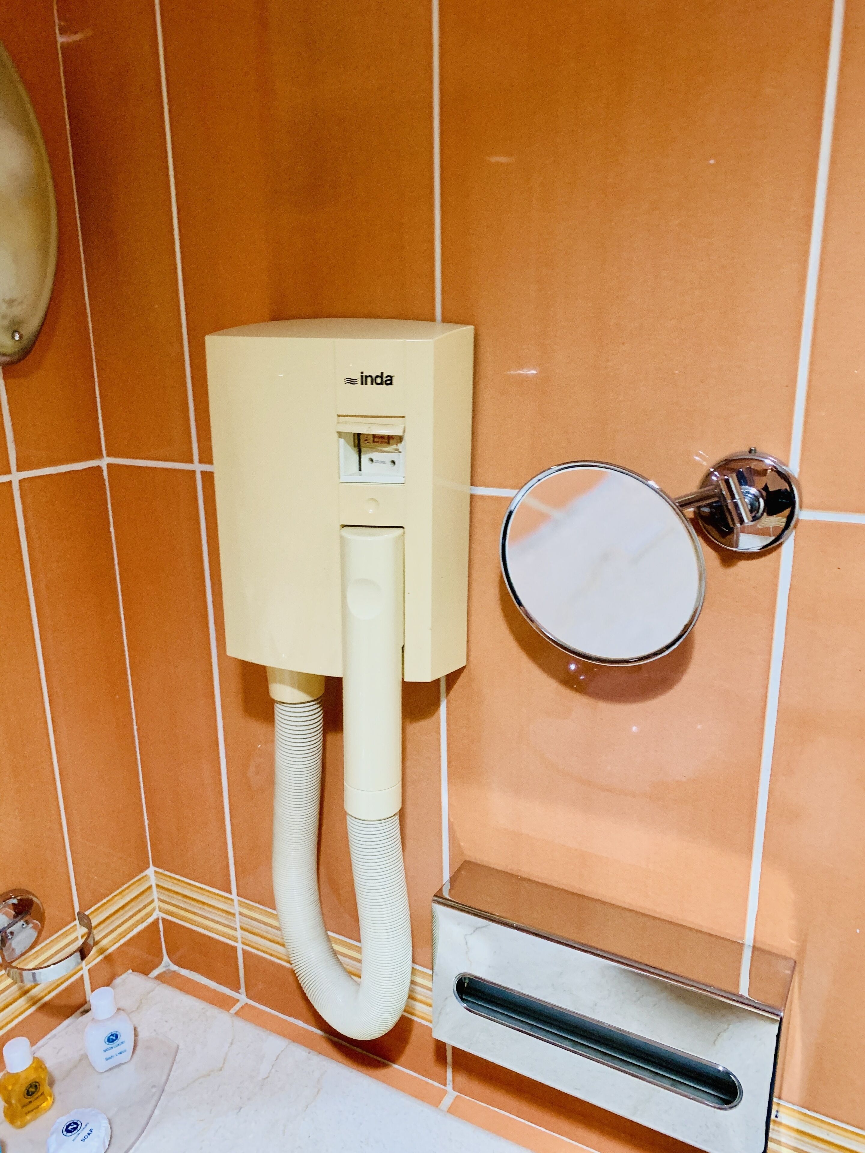 A bathroom with a toilet paper dispenser, a mirror, and a hand dryer.