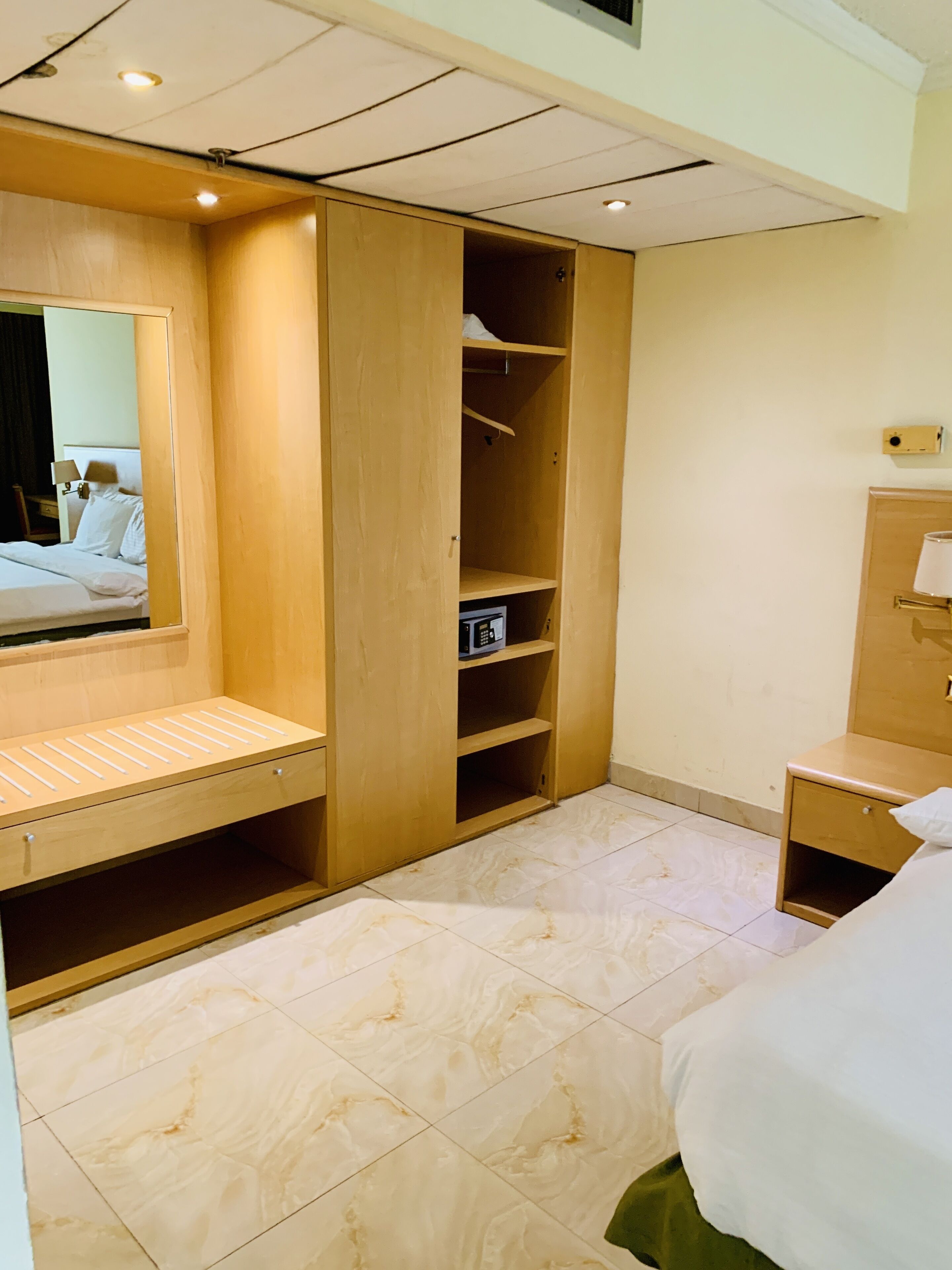 A hotel room with a bed, a wooden wardrobe, a mirror, and a bedside table.