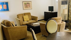 Una habitación de hotel con un juego de sofá, una mesa de comedor, un televisor sobre un mueble y una lámpara.