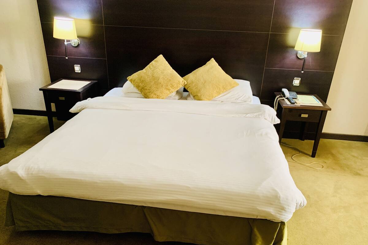 Una habitación de hotel con una cama grande, dos mesitas de noche, un teléfono y lámparas fijadas a la pared.