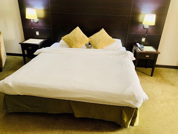 A hotel room with a large bed, two bedside tables, a telephone, and wall-mounted lamps.