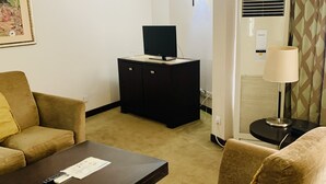 Una habitación de hotel con sofá, mesa de centro, televisor en un mueble, lámpara y aire acondicionado.