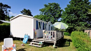 A small, single-story mobile home with a porch, a picnic table, and a small deck. - Mobil-home 3 Chambres 31m² (Telgruc-sur-Mer)