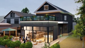 A modern two-story house with a glass balcony, outdoor seating area, and a visible kitchen.