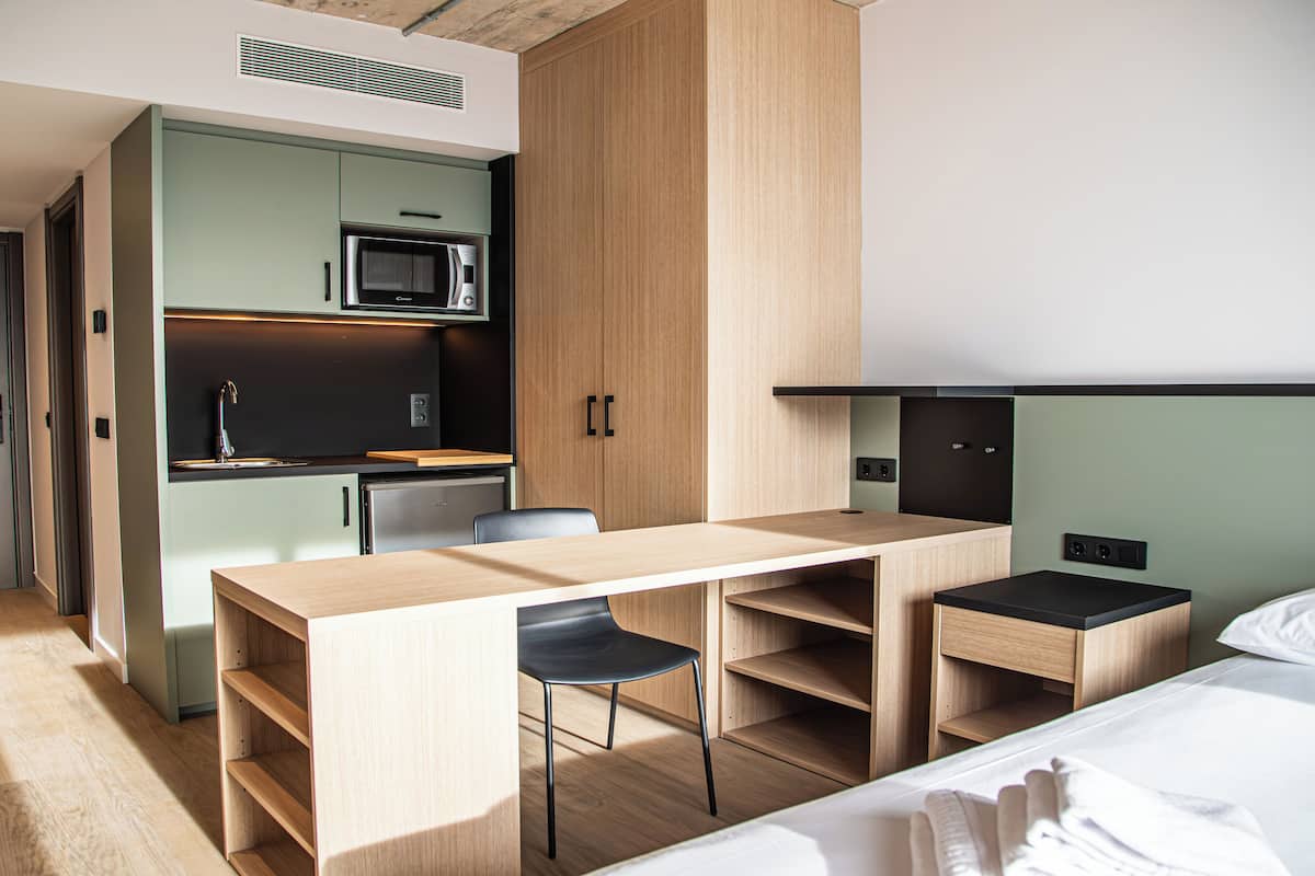 A compact hotel room with a kitchenette, a bed, a desk, and a chair.