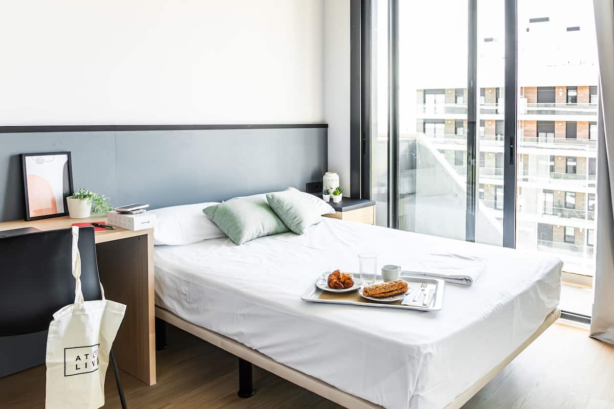 A modern hotel room with a bed, a desk, and a window with a city view.