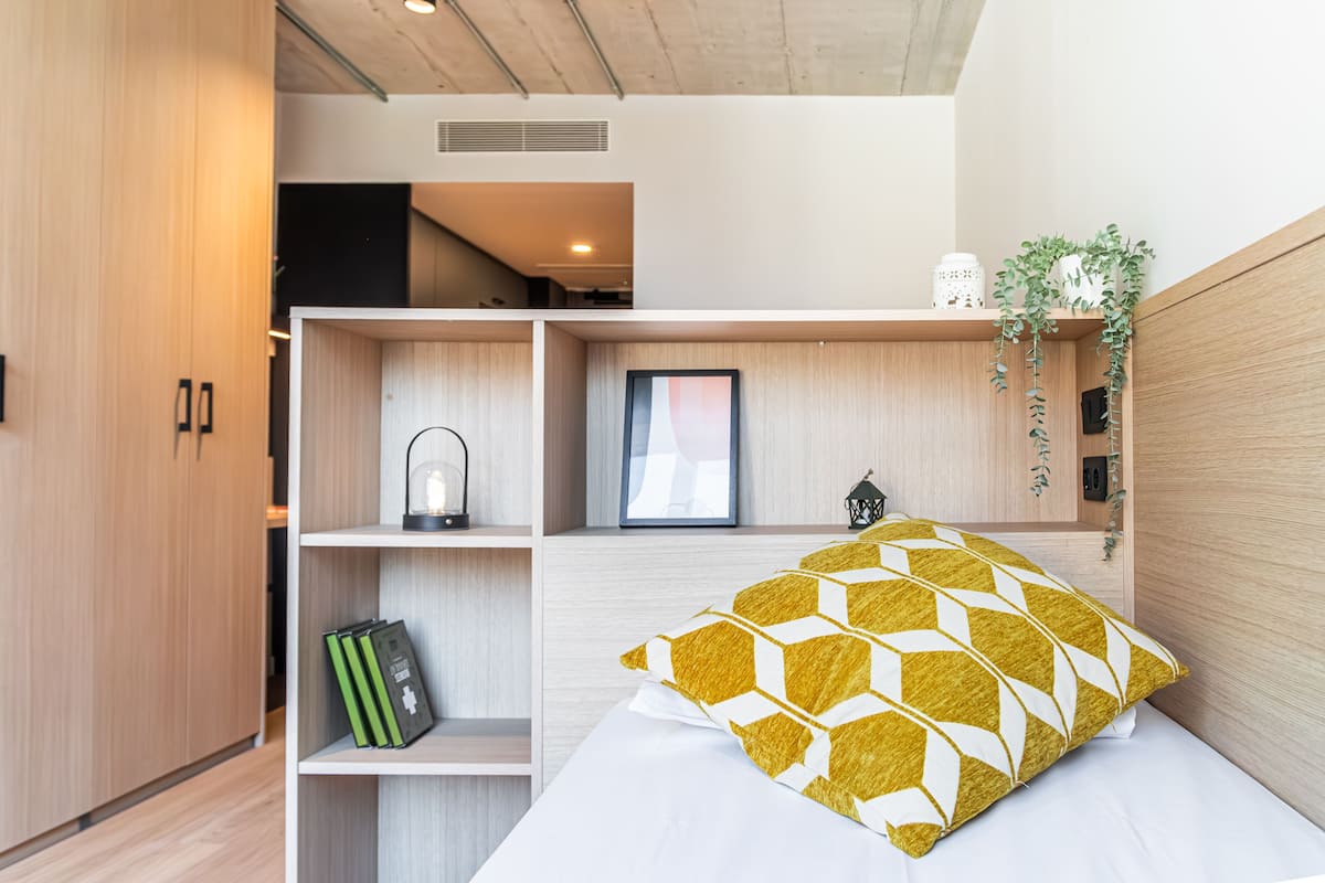 A modern bedroom with a bed, a nightstand, a shelf with books, and a wardrobe.