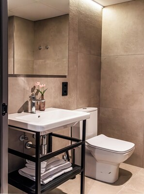 A modern bathroom with a white sink, a mirror, a toilet, and a shelf with towels.