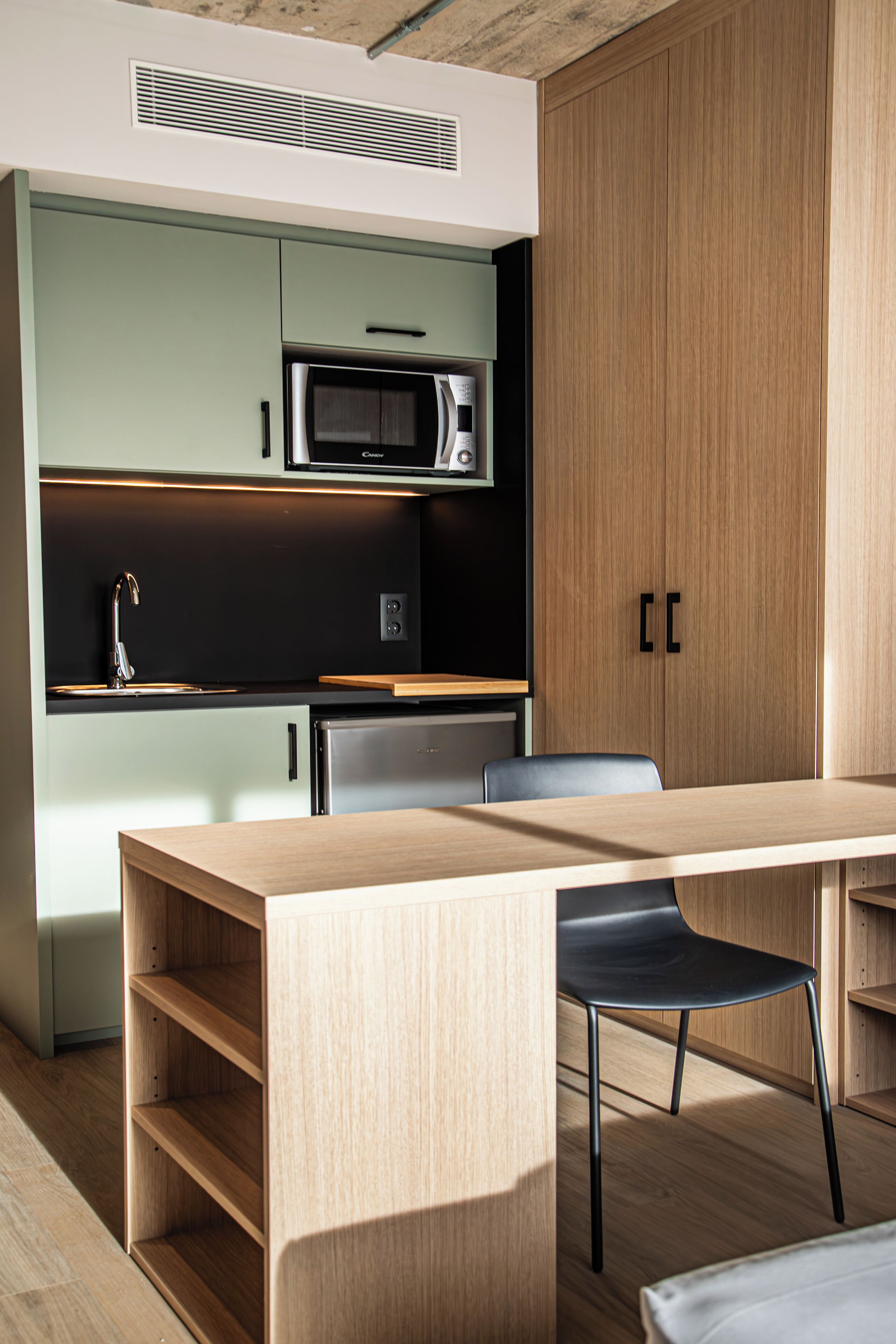 A modern kitchen with a wooden table, a black chair, and built-in appliances.