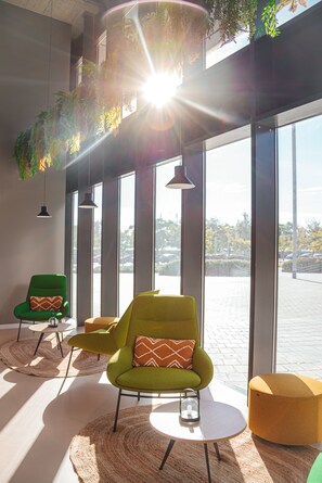 A modern interior with large windows, green and yellow chairs, and hanging plants.