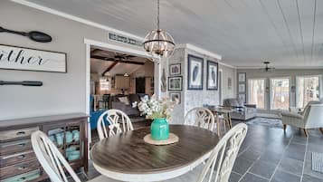 Un coin repas avec une table en bois, des chaises blanches, un vase turquoise orné de fleurs et une pancarte sur laquelle on peut lire : « Bienvenue chez nous ».