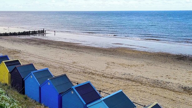 A beach with a row of colorful beach huts and a wooden pier extending into the sea.