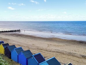 En strand med en rad färgglada strandhytter och en träbrygga som sträcker sig ut i havet.