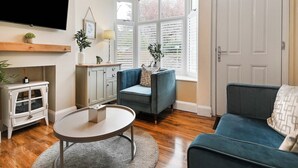 A living room with a TV mounted on the wall, a sofa, a coffee table, and a cabinet with a plant.