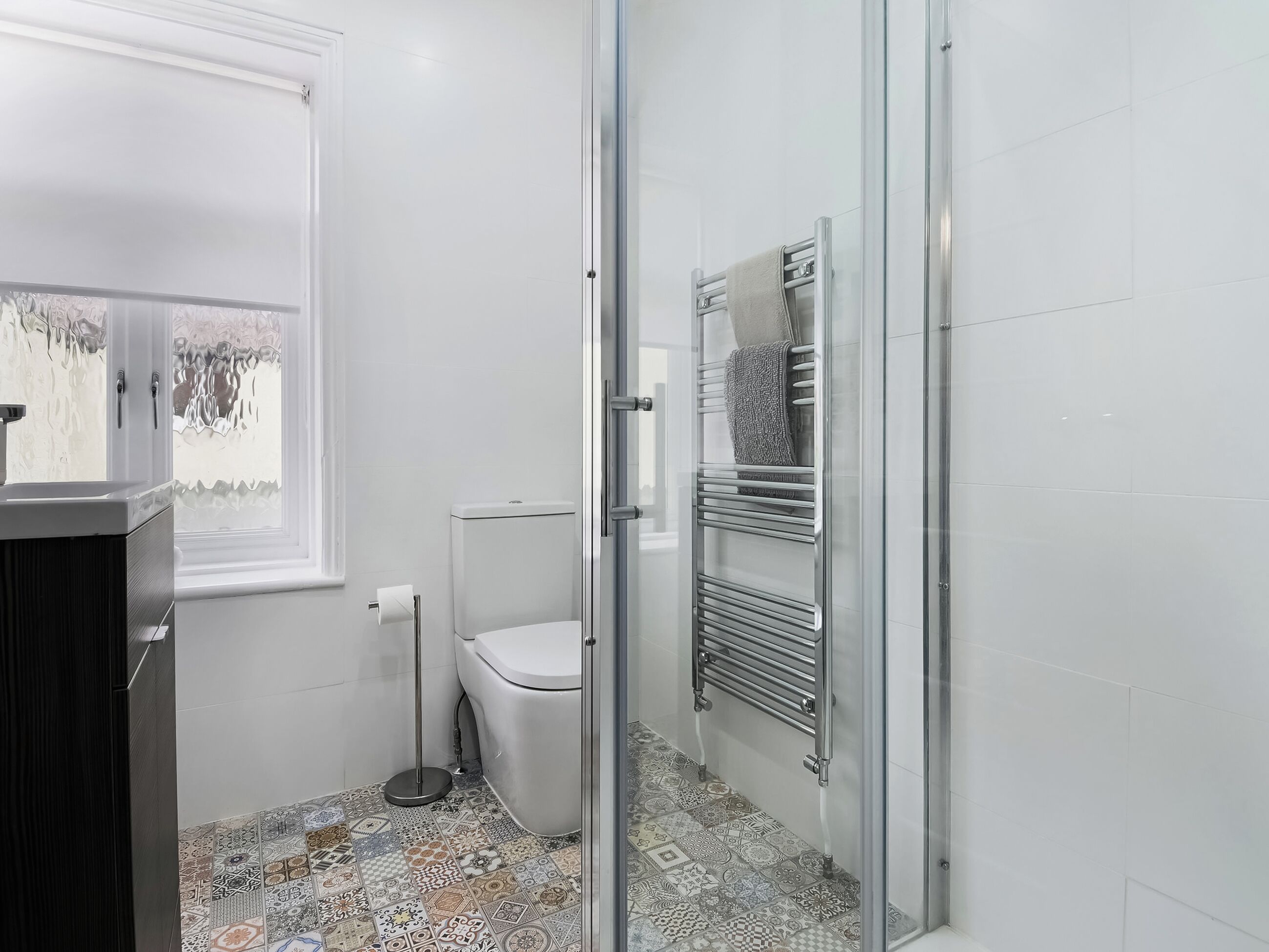 Une salle de bain comprenant des toilettes, une douche en verre, un porte-serviettes et des carreaux de sol à motifs.