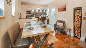 A modern kitchen with stainless steel appliances, a dining area with a wooden table set for four, and a cozy seating area with a plaid armchair.
