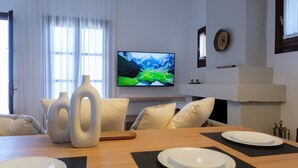 Een moderne woonkamer met een houten eettafel voor vier personen, witte borden en een flatscreen televisie waarop een mooi landschap te zien is.