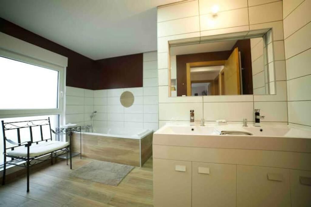 Un baño moderno con un espejo grande, una bañera y un banco.
