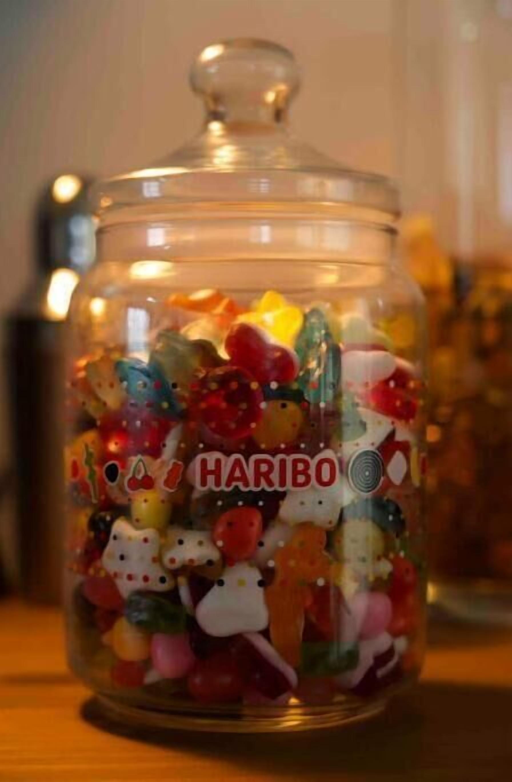 A glass jar filled with colorful candies, labeled "HARIBO," on a wooden surface.